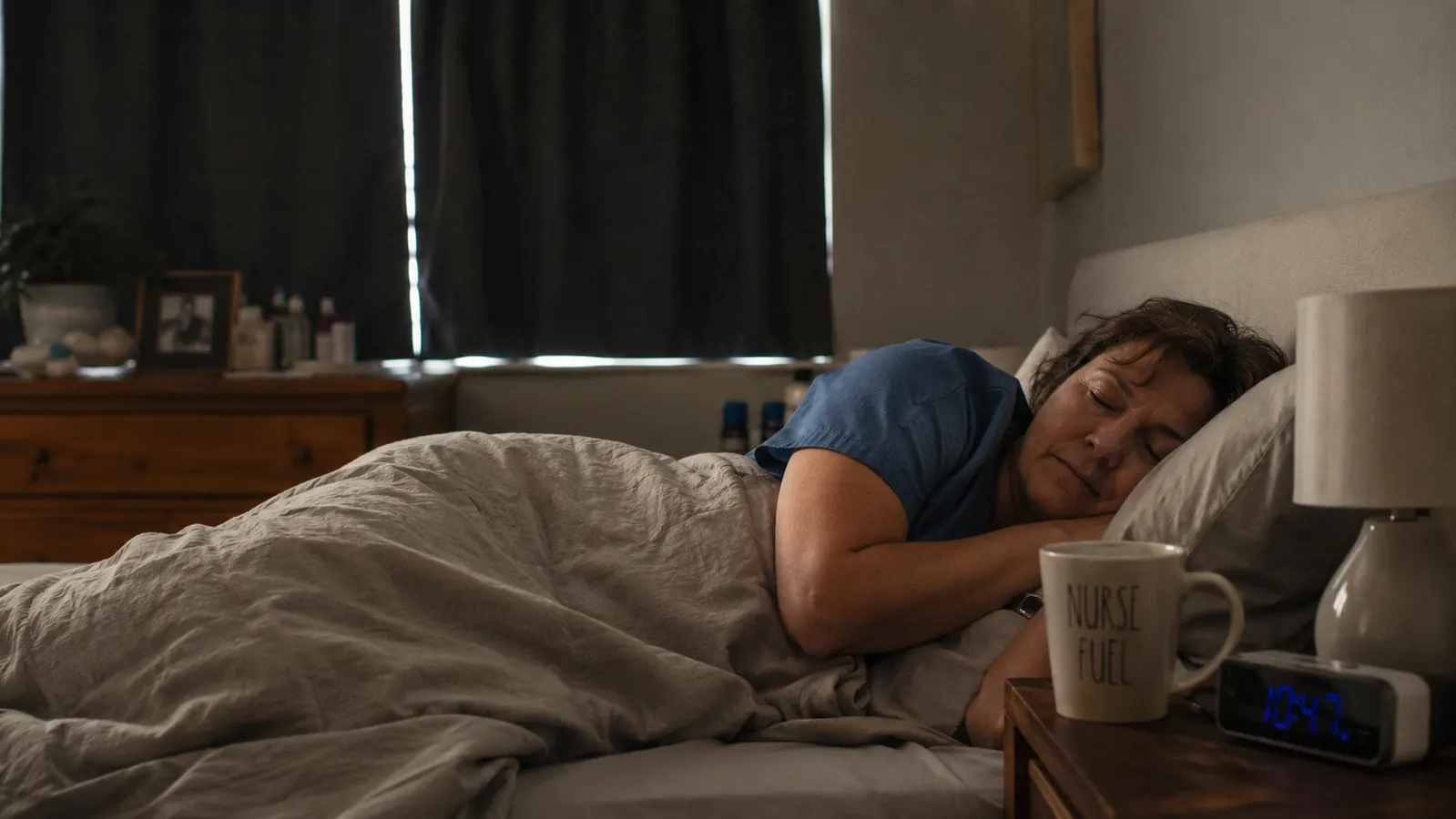 Woman in a darkened bedroom during the day, wearing a soft fabric headband with speakers, drifting off to sleep