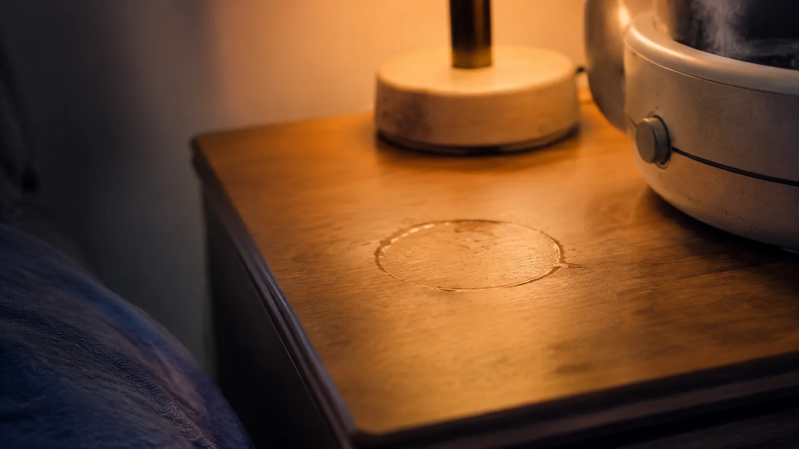 Close view of a faint water ring in the finish of a wood dresser next to a small humidifier with no mat underneath