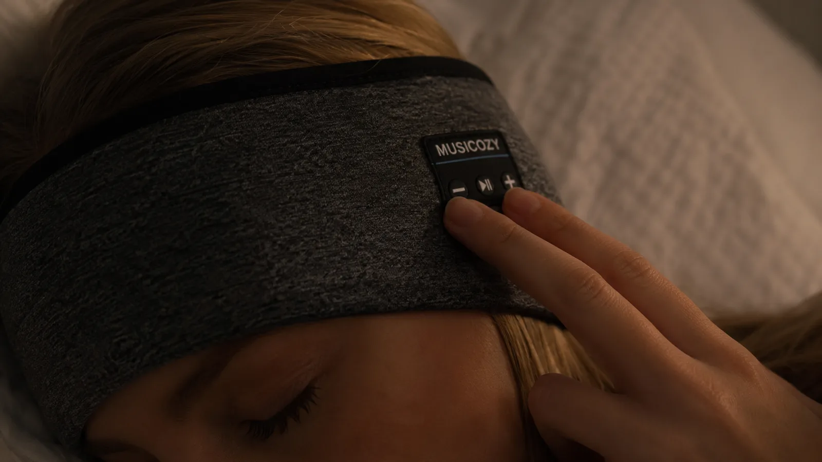 Close-up of a hand feeling along the flush fabric-covered buttons on the side of a sleep headband in dim light